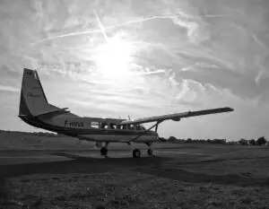 Petit avion Cessna Caravan utilisé pour le parachutisme stationné sur une piste, photographié en noir et blanc avec le soleil bas dans le ciel.