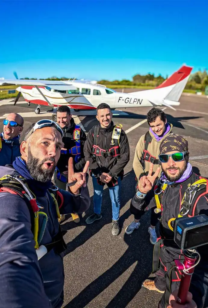 Plusieurs personnes équipées de harnais de parachutisme posant ensemble devant un petit avion sur le tarmac.