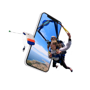 Duo en parachute semblant sortir de l’écran d’un smartphone, avec la voile déployée à gauche.
