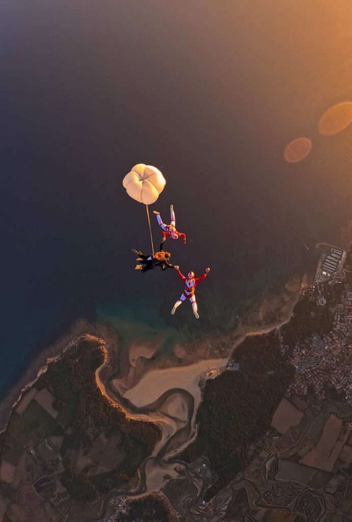Les Airwax en chute libre avec un tandem dont le RSE est déployé, au‑dessus du Veillon éclairé par la lumière dorée du coucher du soleil.