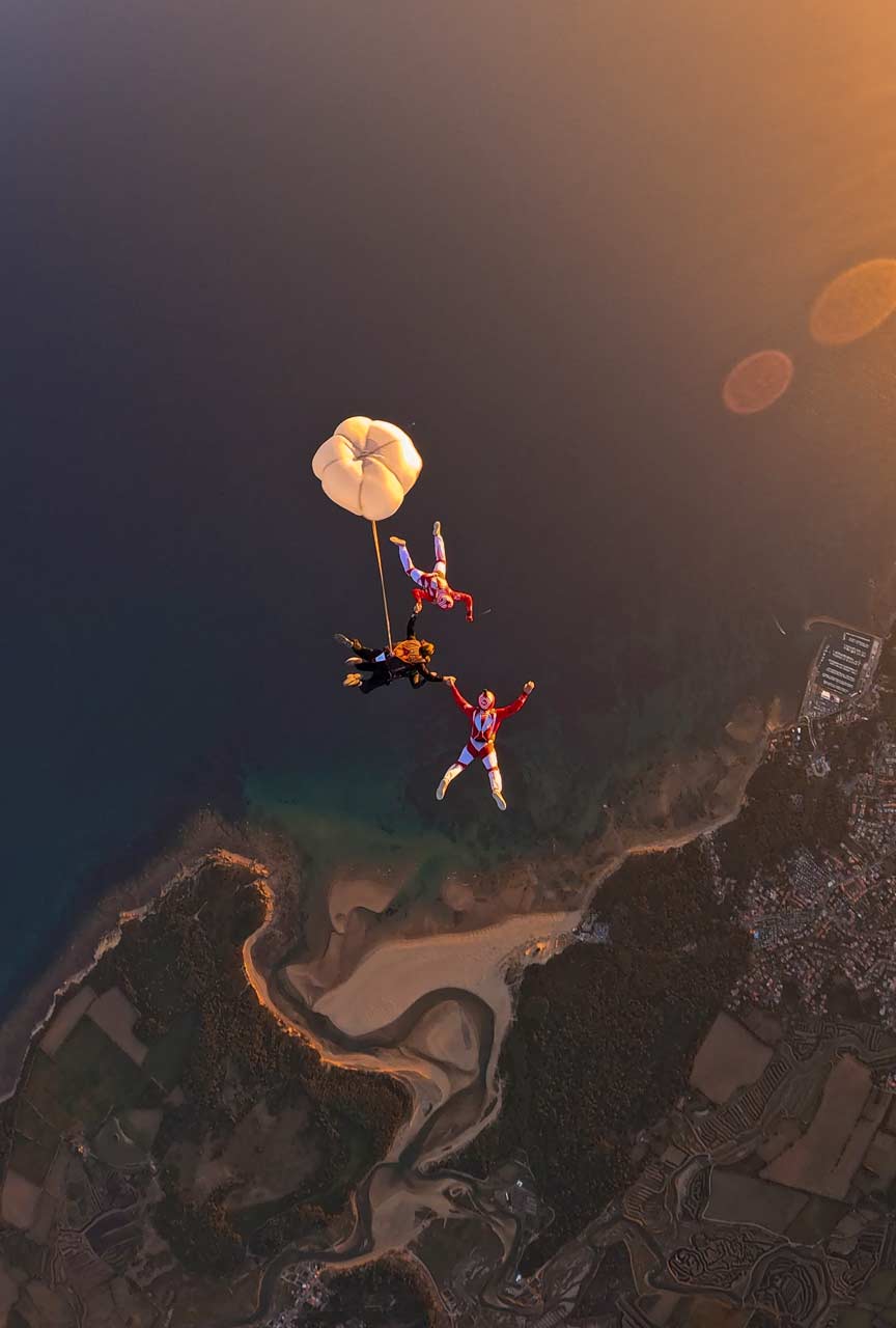 Les Airwax en chute libre avec un tandem dont le RSE est déployé, au‑dessus du Veillon éclairé par la lumière dorée du coucher du soleil.